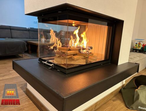 Ofen mit Feuertisch als schlichter Raumtrenner mit dreiseitigem Fenster, um von allen Seiten einen Blick auf das Feuer zu bekommen.