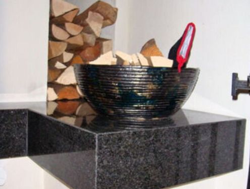 Ein zweiseitiger Ofen mit schwarzer Sitzbank und Holznischen für Brennholz und Dekoration