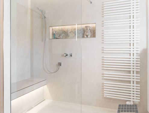Ein helles und freundliches Badezimmer mit Waschtisch aus Holz und Duschbank mit indirekter Beleuchtung