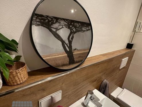Ein extravagantes Badezimmer. Die Holzoptikfliesen und weißen Fliesen sind zwar schlichter gehalten, doch durch die ganzflächige Fototapete wird das Badezimmer zur Savanne.