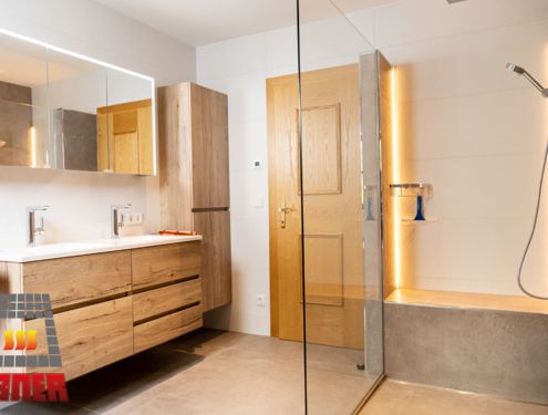 Modern, zeitlos und im Landhausstil. Durch die schlichten Fliesenfarben und den Badezimmermöbeln aus Holz wirkt das Badezimmer gemütlich und freundlich.