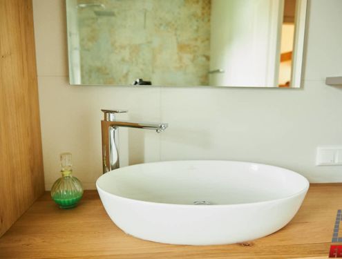 Badezimmer mit Dekorfliese im Großformat und schlichtem Waschtisch aus Holz